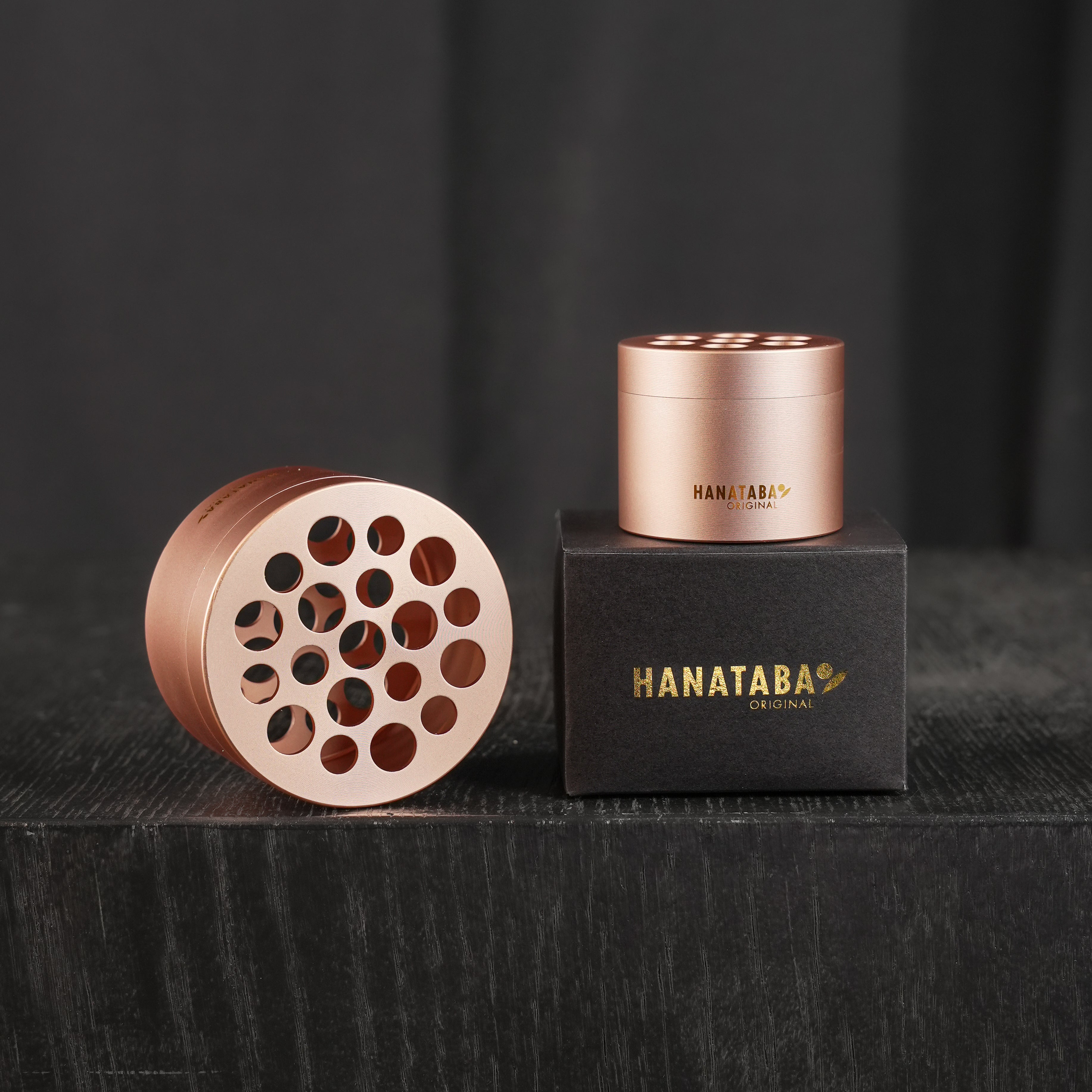 Two Hanataba bouquet twisters in pink champagne, one atop its elegant black box with gold lettering, sit on a dark surface, showcasing the stylish design and functionality of flower arranging tools.