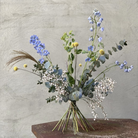 Ekspozycja kwiatowa Ikebana z niebieskimi delphiniums, żółtymi craspedia i delikatnym oddechem dziecka, ułożona przy użyciu tradycyjnego spiralnego uchwytu Hanataba z japońskimi technikami.